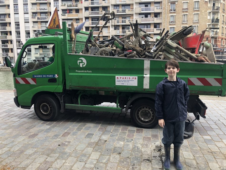 young boy Rafael Marinho stands in front of green dump truck full of metal waste