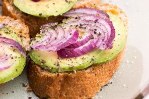 Open-faced toast topped with avocado slices and red onion, lightly seasoned with cracked pepper and salt.