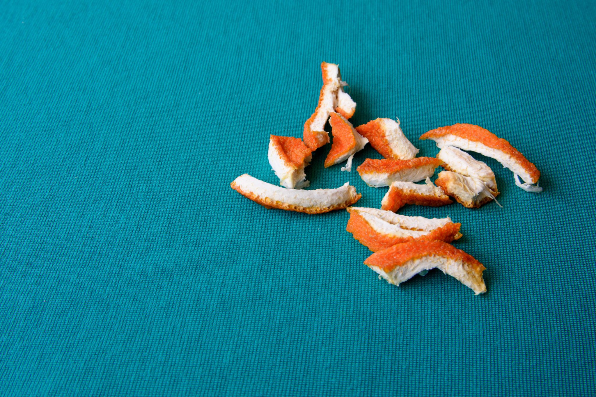 Pieces of orange peel scattered on a bright teal fabric background.