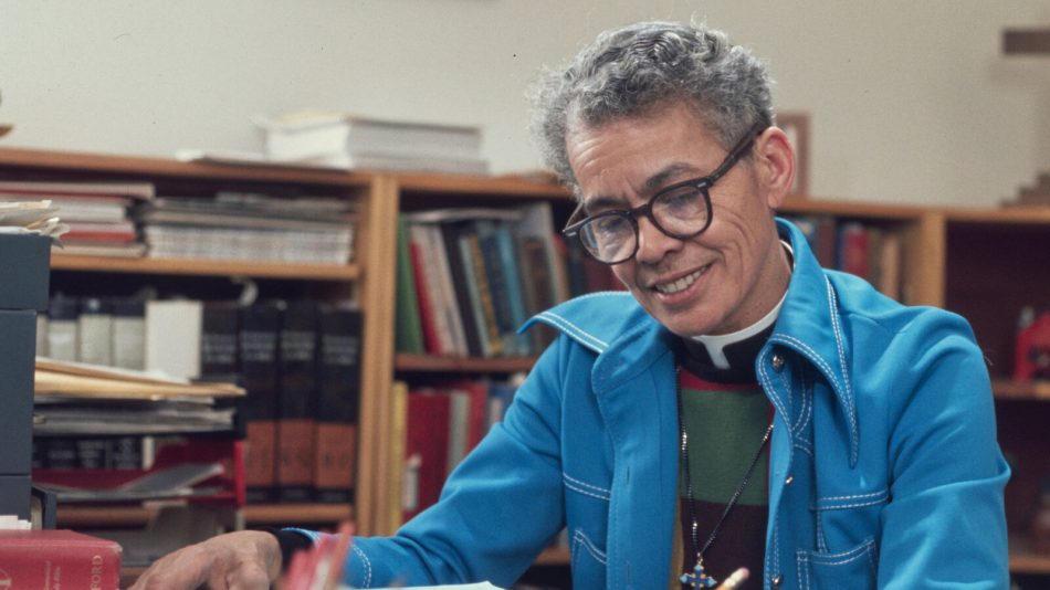 Snapshot from the documentary “My Name Is Pauli Murray.” She sits with a blue jacket wearing glasses writing.