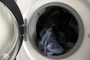 Front-loading washing machine with the door open and denim jeans in the drum.