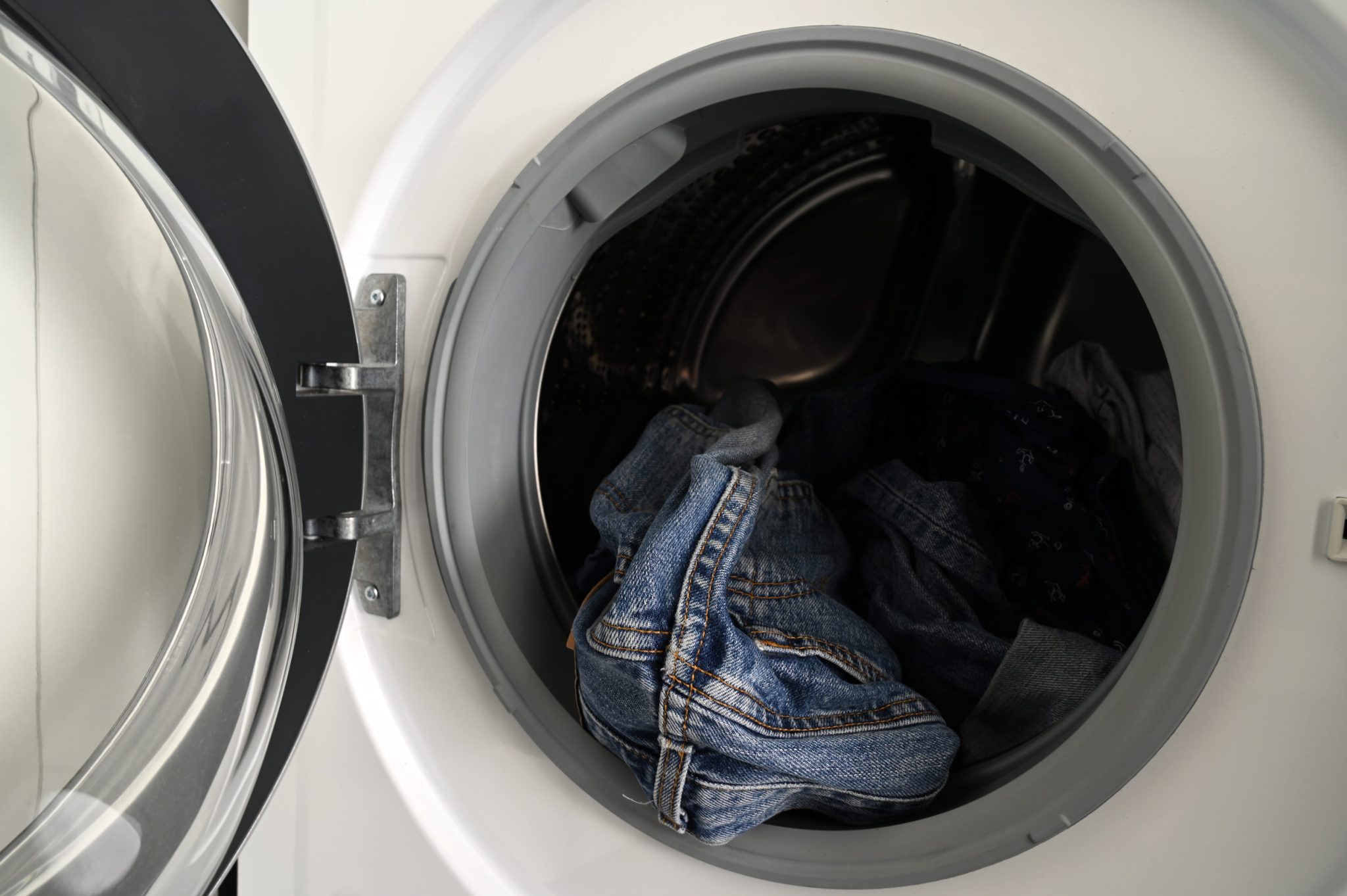 Front-loading washing machine with the door open and denim jeans in the drum.