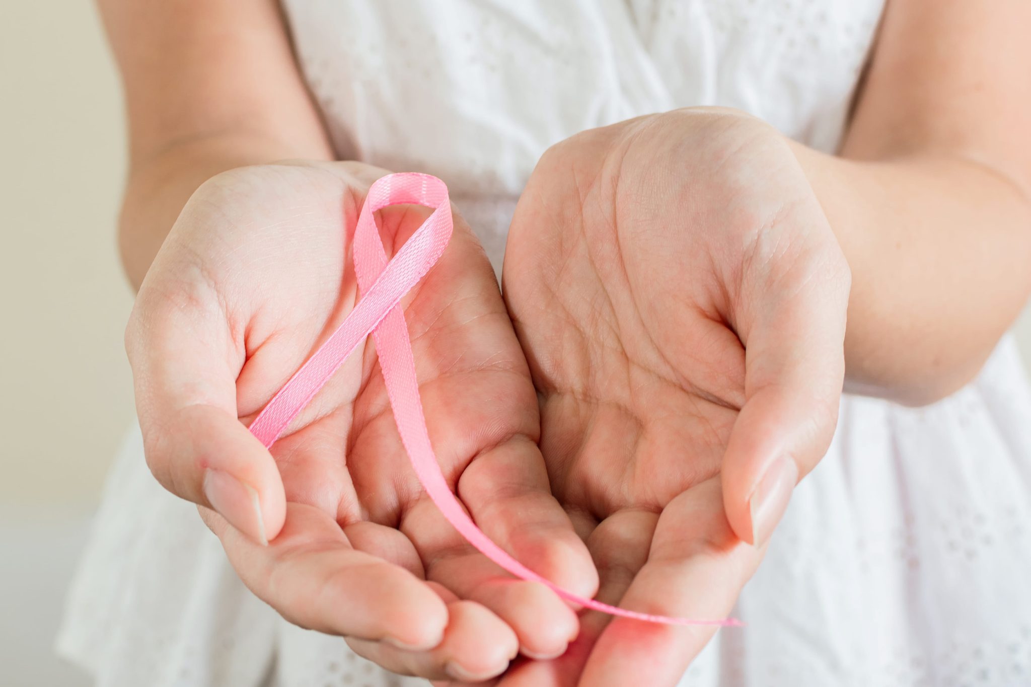 Close-up of hands cupping a pink ribbon symbolizing breast cancer awareness.