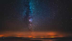 Night sky filled with stars and the Milky Way, above an orange-lit horizon.