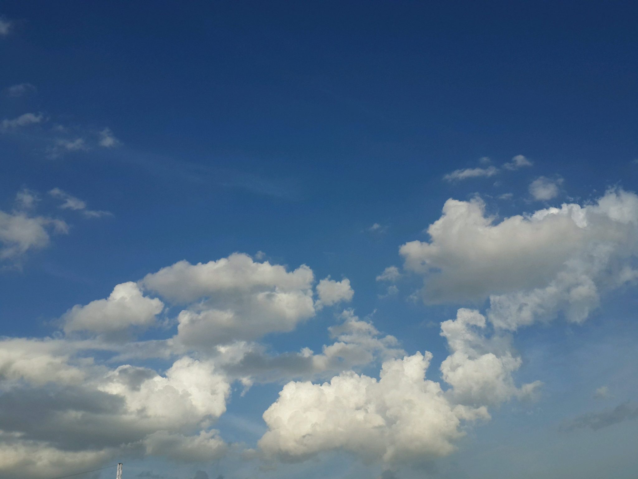Blue sky with scattered white clouds and a small pole visible at the bottom-left edge.
