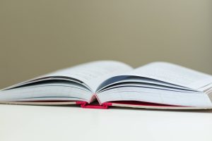 Open book lying flat on a white surface, pages spread wide with a red bookmark ribbon visible at the bottom edge of the book