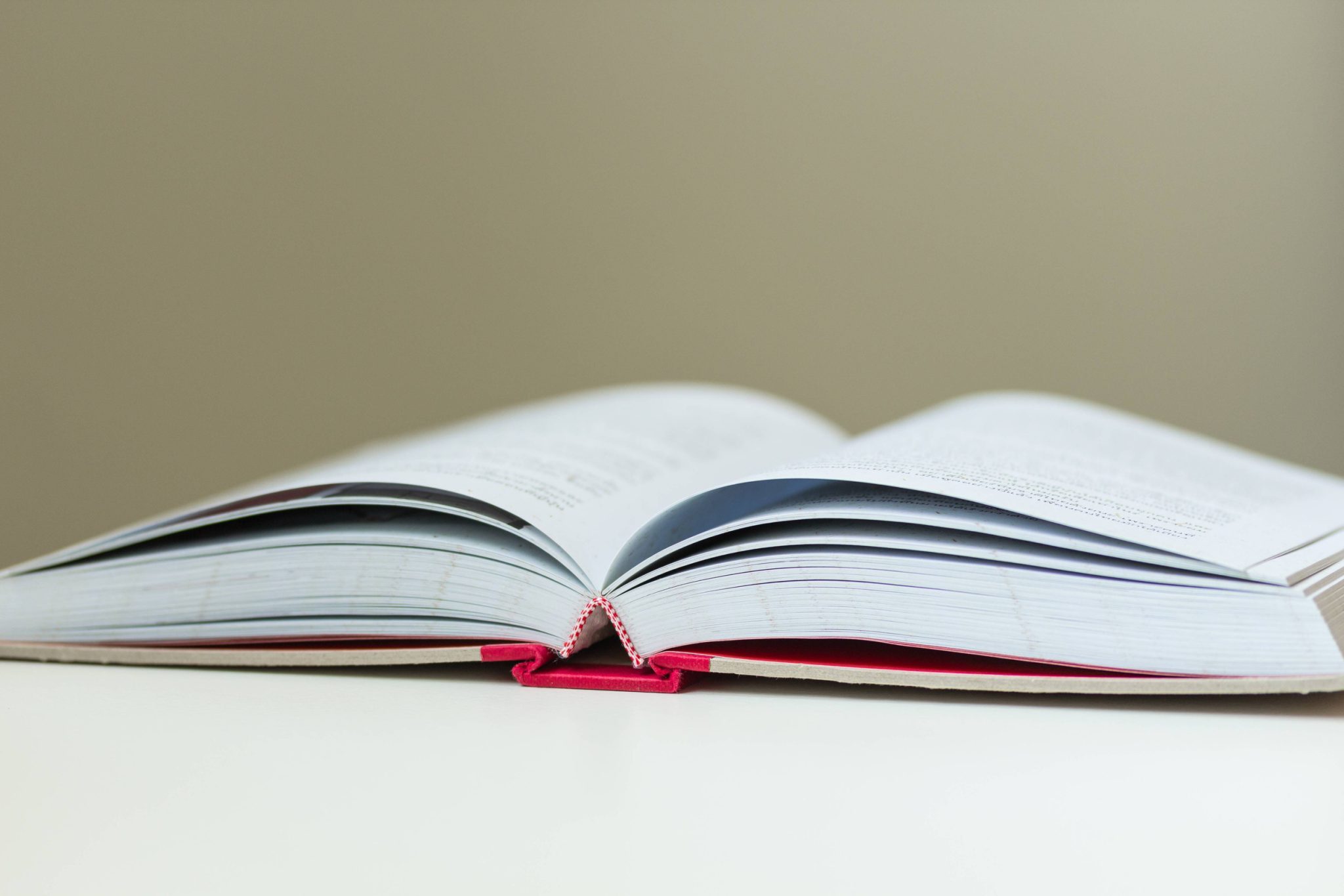 Open book lying flat on a white surface, pages spread wide with a red bookmark ribbon visible at the bottom edge of the book