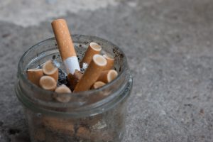 Jar filled with cigarette butts and ash on a rough surface, close-up view.