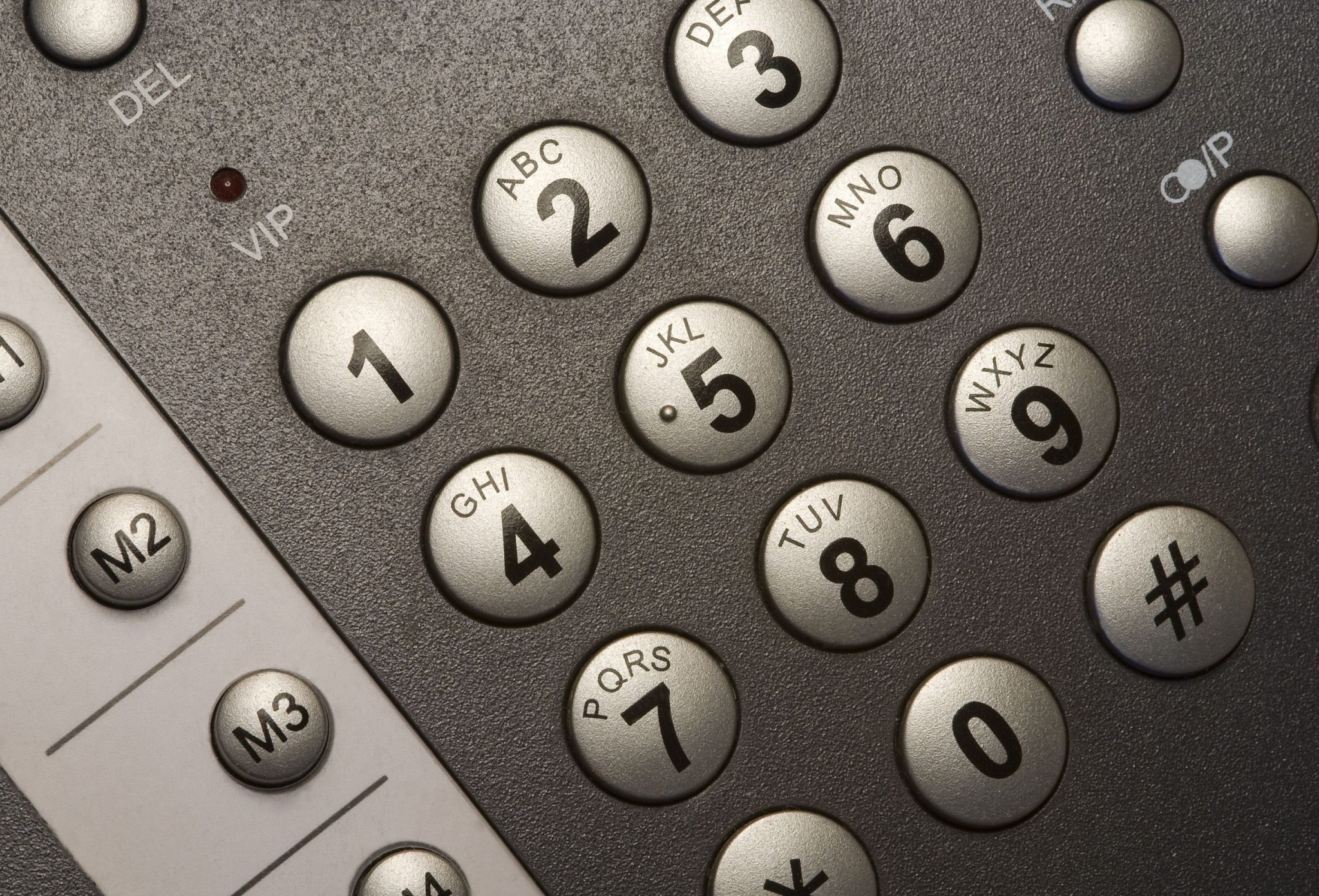 Close-up of a keypad with round gray number keys labeled with letters (2–9) and adjacent function keys visible on a textured surface