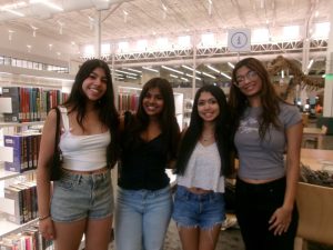 KODAK Digital Still Camera | The Optimist Daily: Making Solutions the News Four young women pose together and smile in a bookstore near book shelves and a dinosaur display in the background.