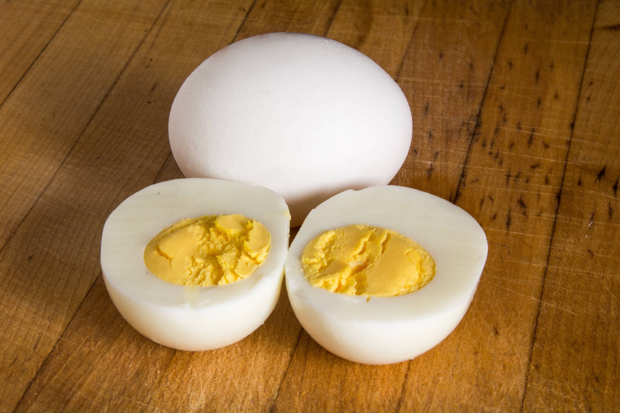 Three hard-boiled eggs on a wooden surface: one whole egg and two halved eggs with yellow yolks exposed.