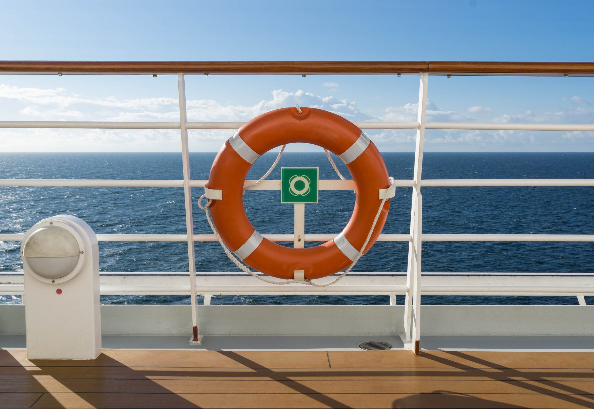 Orange lifebuoy mounted on a ship railing with the sea and blue sky behind it, signifying maritime safety.