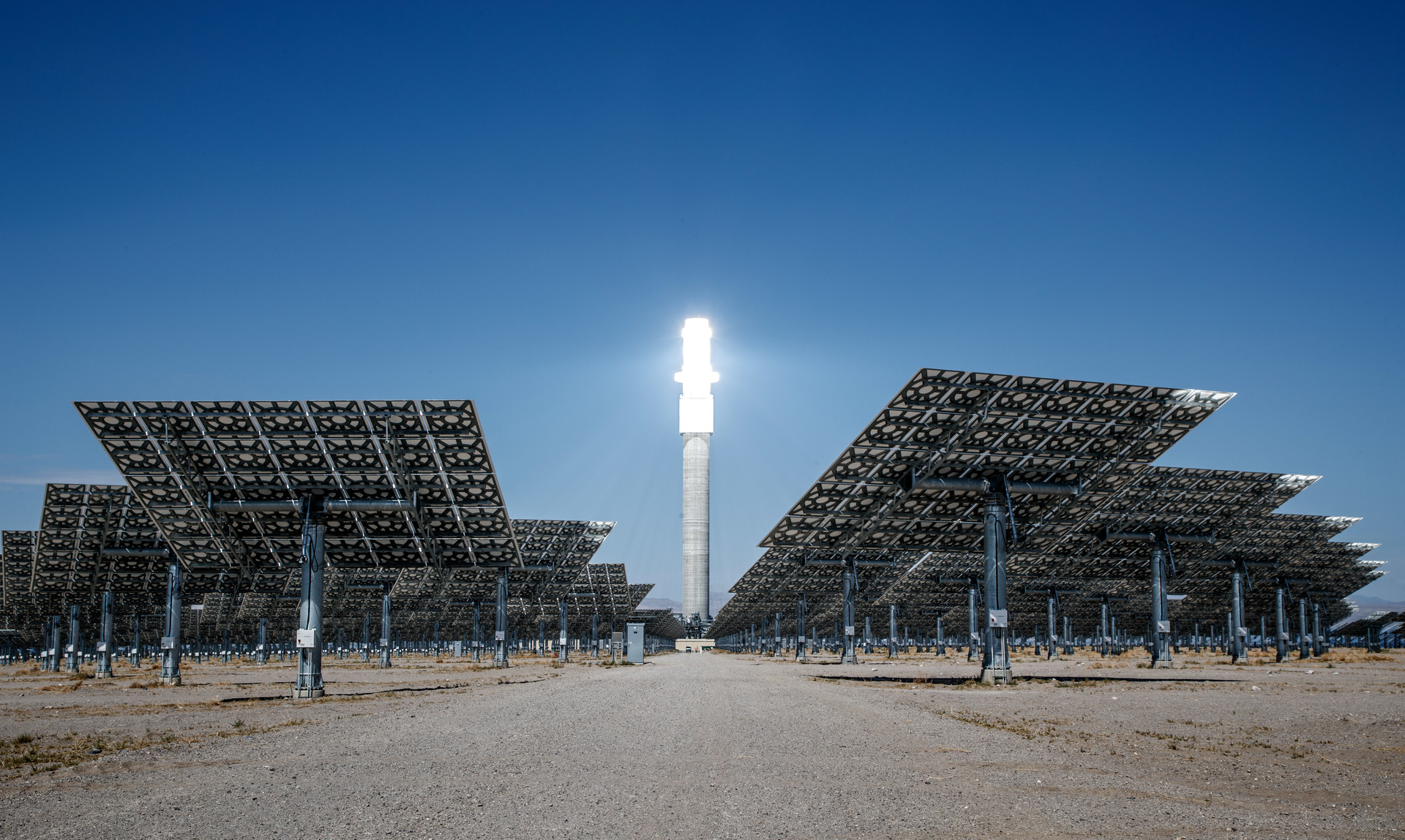 Desert solar thermal plant with hundreds of heliostat mirrors surrounding a tall central receiver tower.