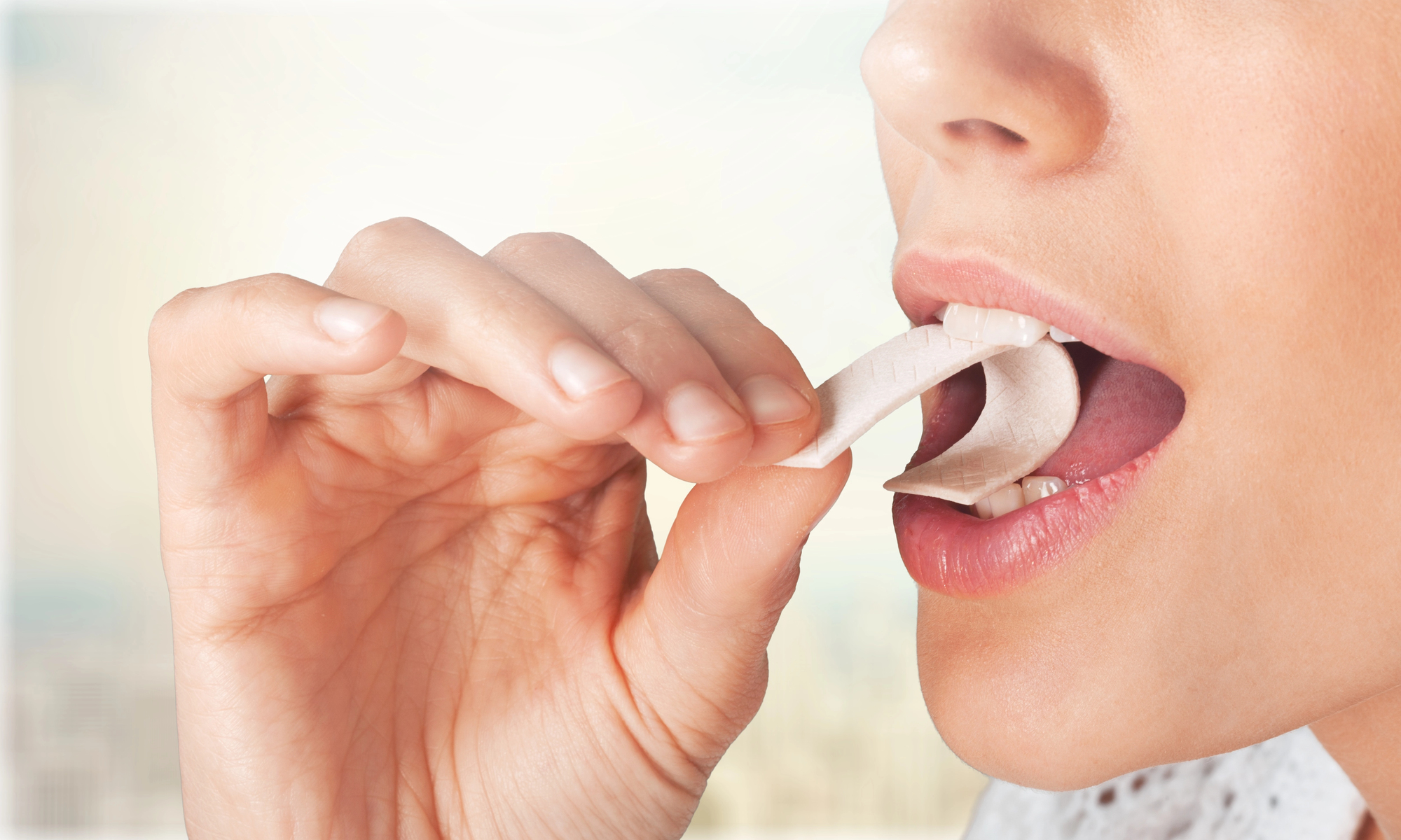 Close-up of a person applying a white dental whitening strip to their teeth while biting down gently on it