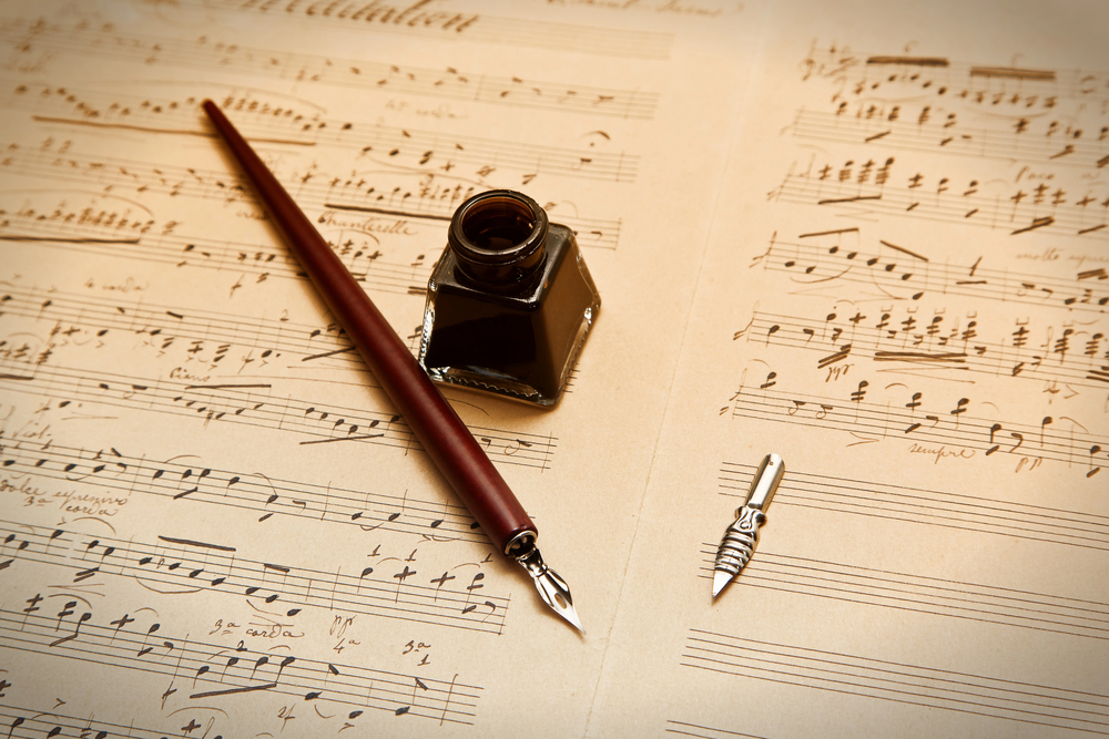 Vintage music sheets with a red fountain pen, an ink bottle, and a spare nib on parchment-like paper.