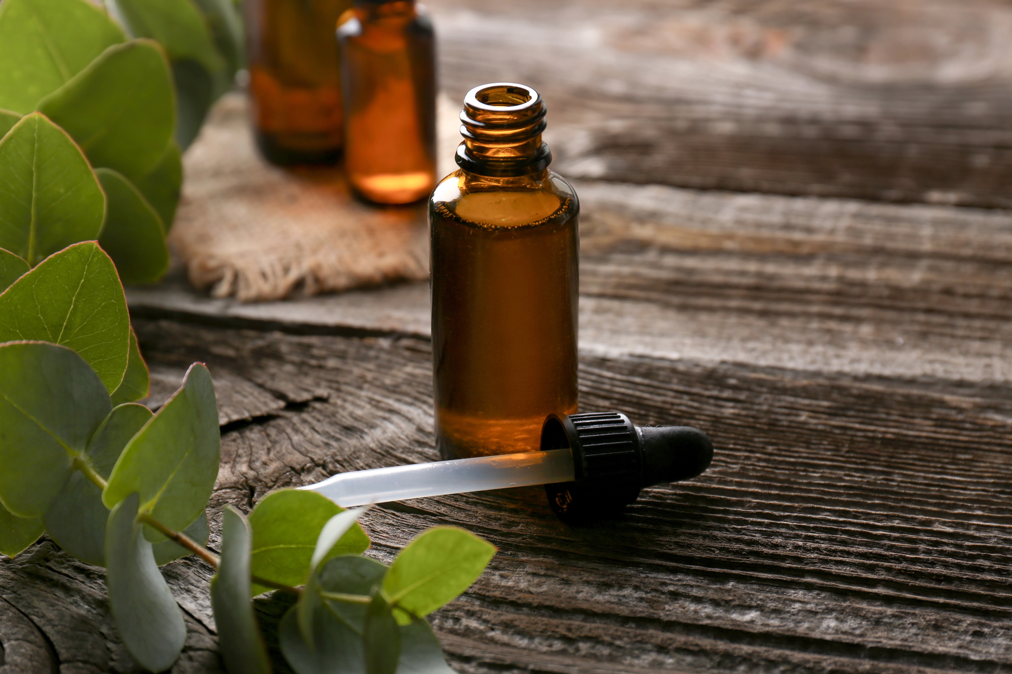 Amber glass essential oil bottle with dropper on a weathered wooden surface, with green leaves in the foreground.