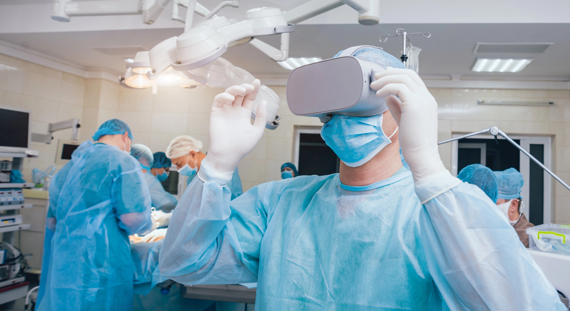 Surgeon wearing a virtual reality headset and surgical mask during surgery, with team in blue gowns working in the background.