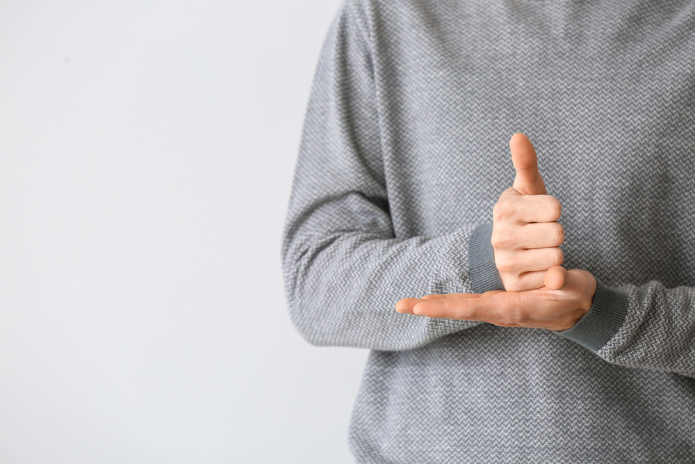 Person in a gray knit sweater making a shaka gesture with thumb and pinky extended