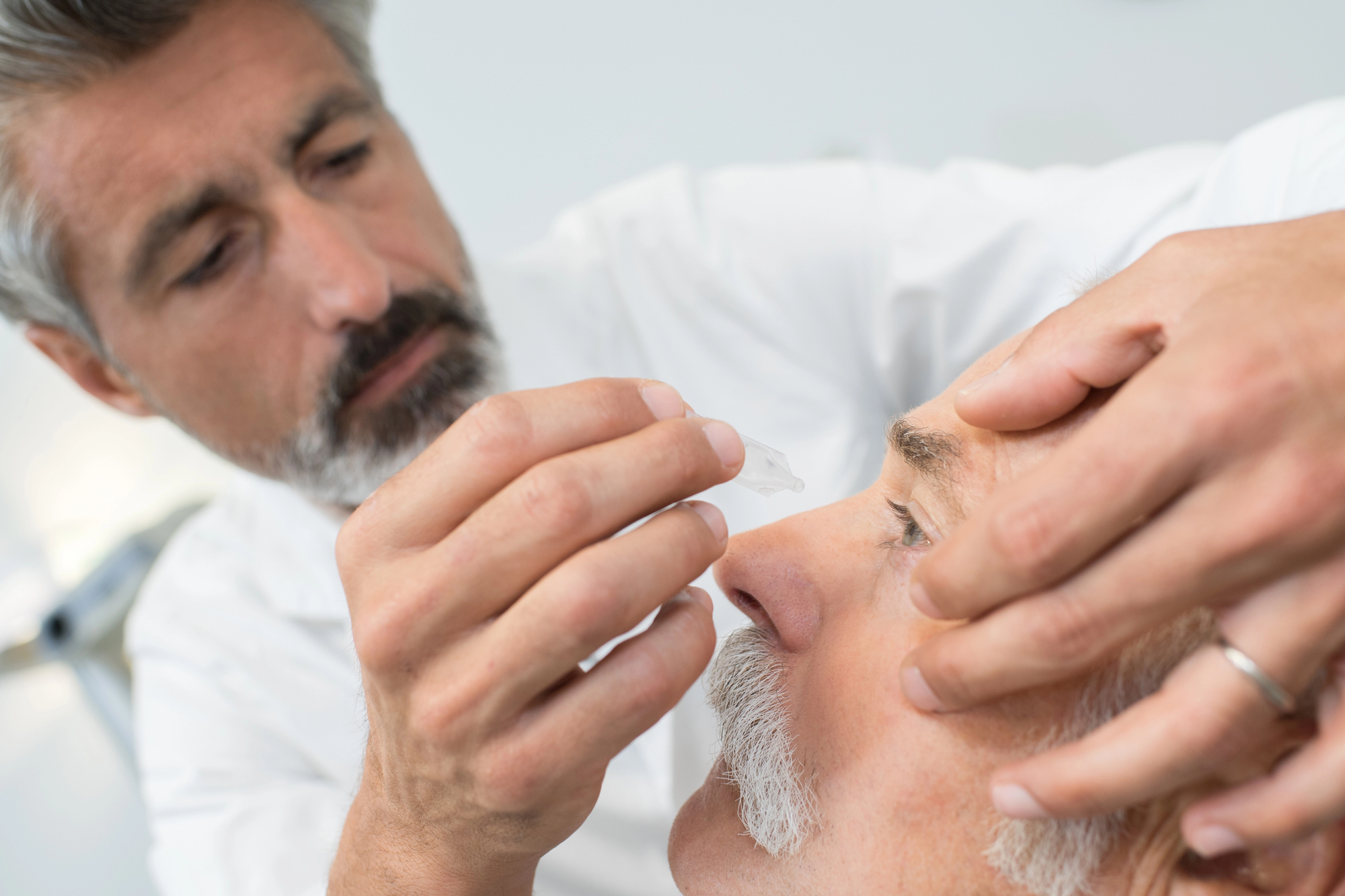 Medical professional administers a facial injection to an older man who is lying down.