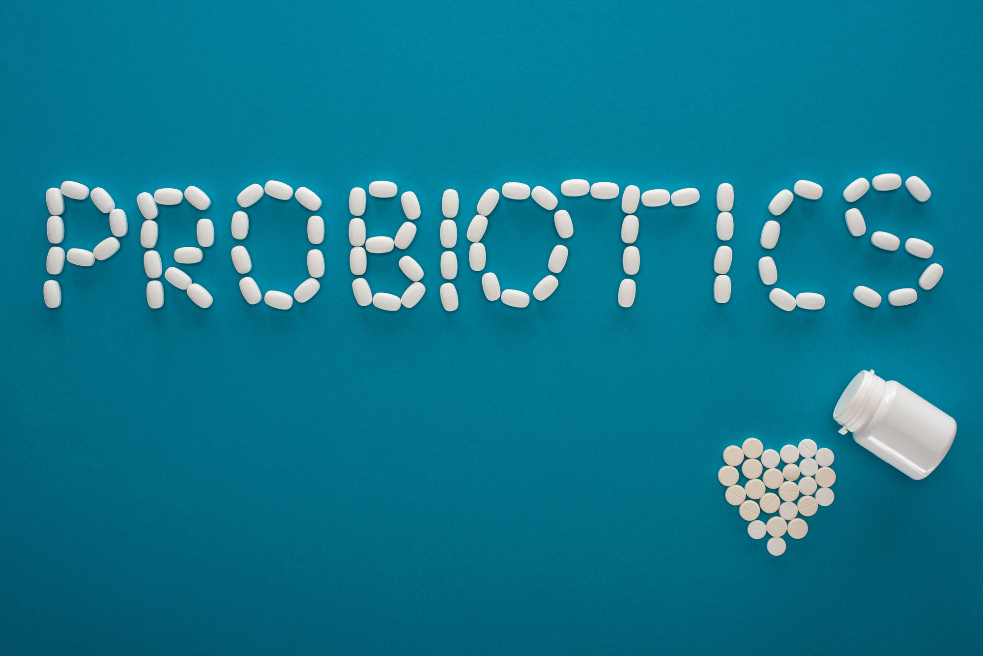 Pills arranged to spell 'DRUGS' on a teal background with an open bottle and scattered tablets nearby.