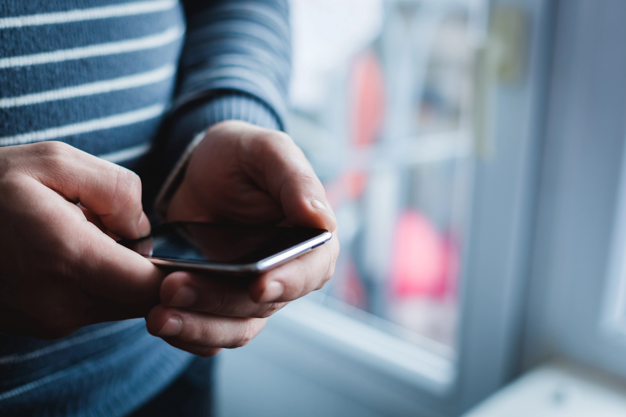 Person holding and using a smartphone, close-up of hands in a striped sweater sleeve in focus, blurred background