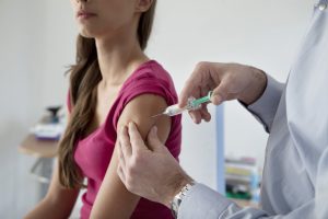 Woman receives an injection in her upper arm from a healthcare professional in a clinical setting.