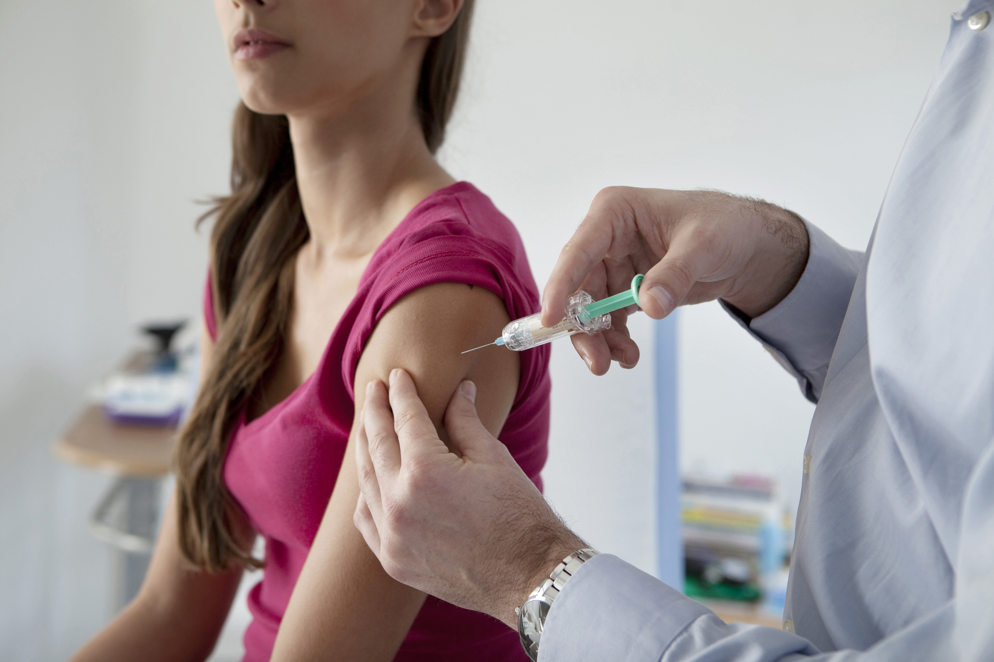 Woman receives an injection in her upper arm from a healthcare professional in a clinical setting.