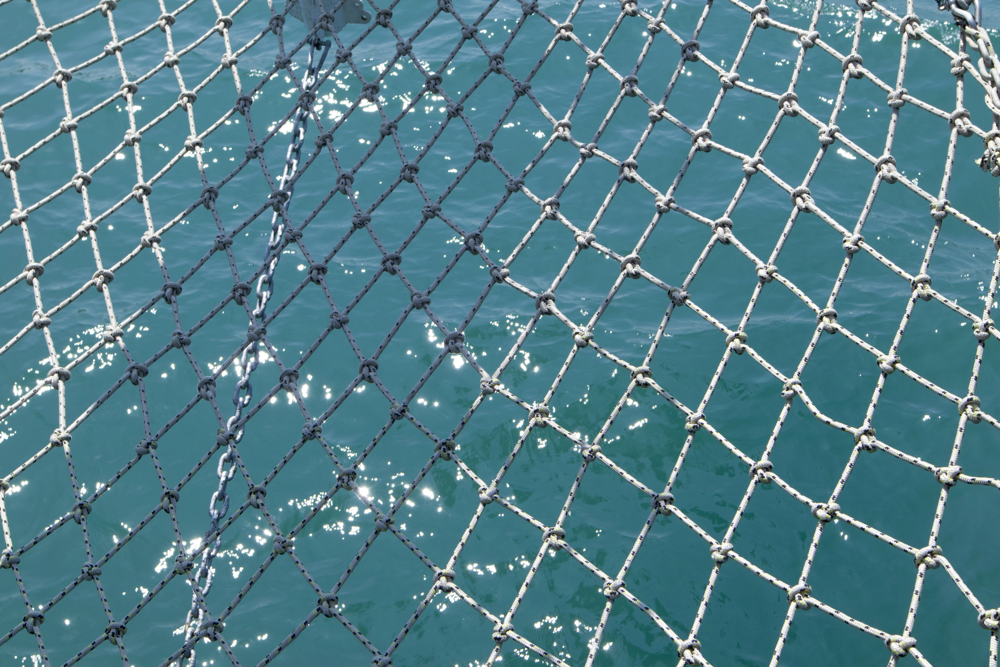 Close-up of a knotted fishing net stretched over turquoise water.