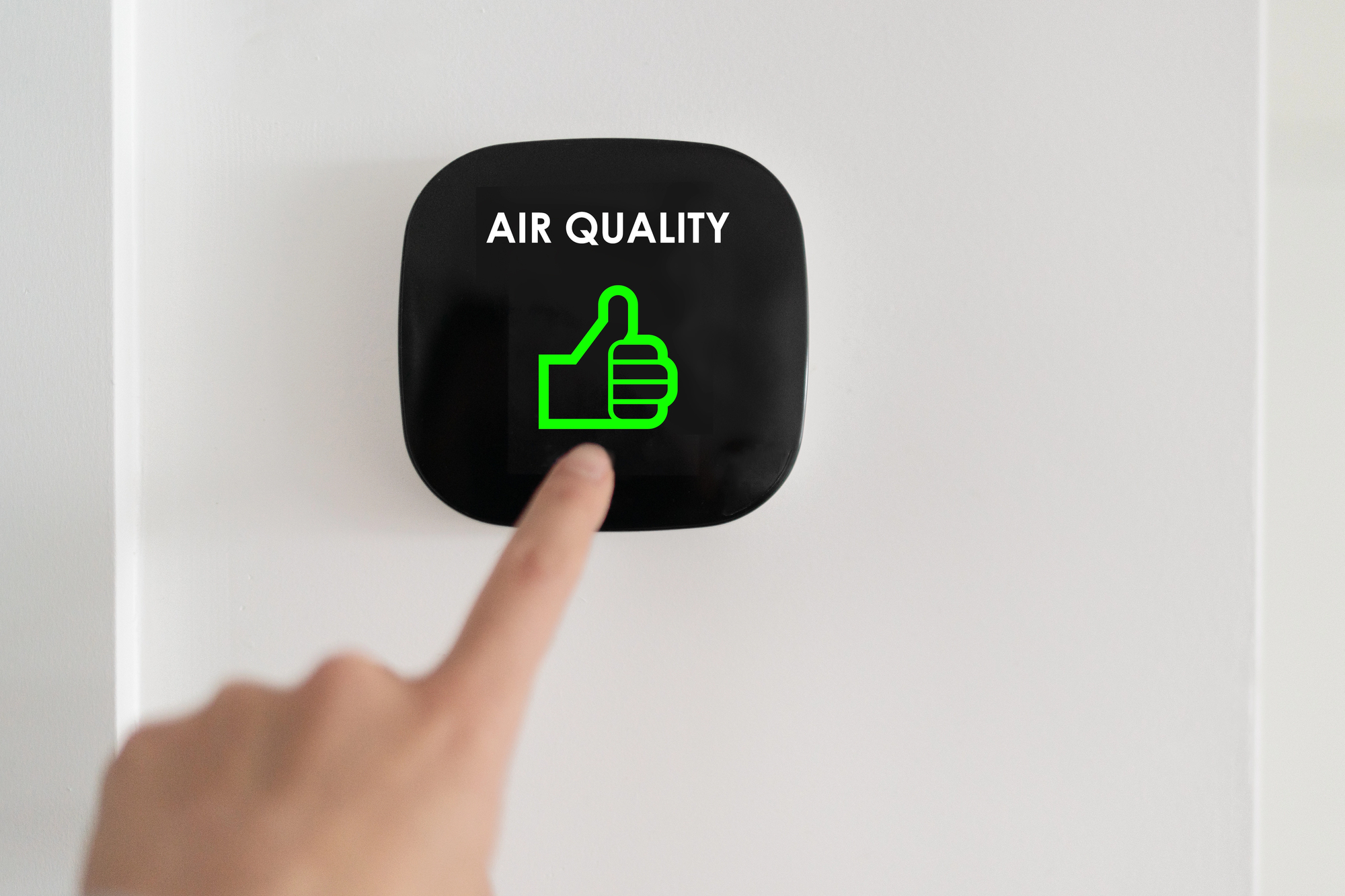 Finger pressing a black square air-quality device labeled 'AIR QUALITY' with a bright green thumbs-up icon.