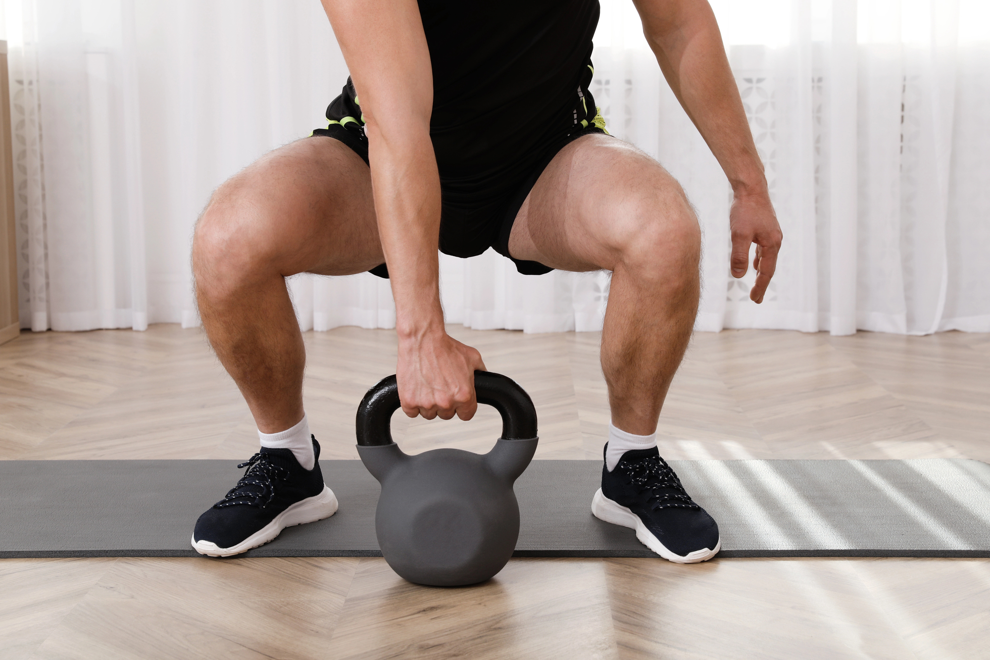 Person in black athletic wear performing a kettlebell goblet squat on a workout mat indoors.