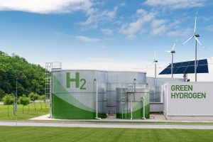 Green hydrogen energy site with large H2 storage tank, solar panels, and wind turbines under a blue sky
