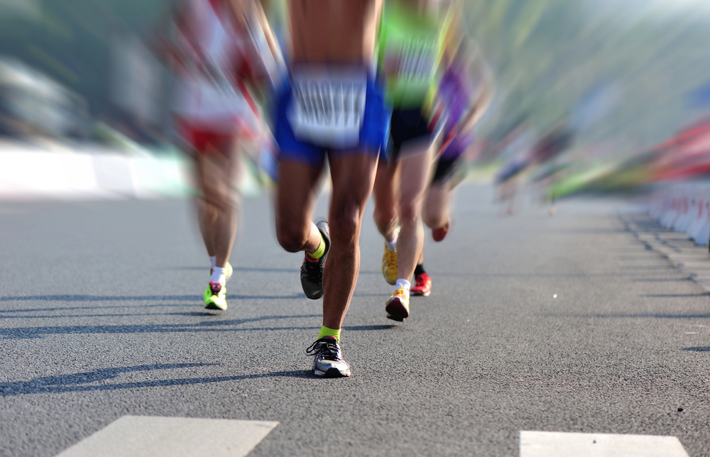 A group of runners sprinting on a city street during a road race, viewed from ground level with a blurred background.