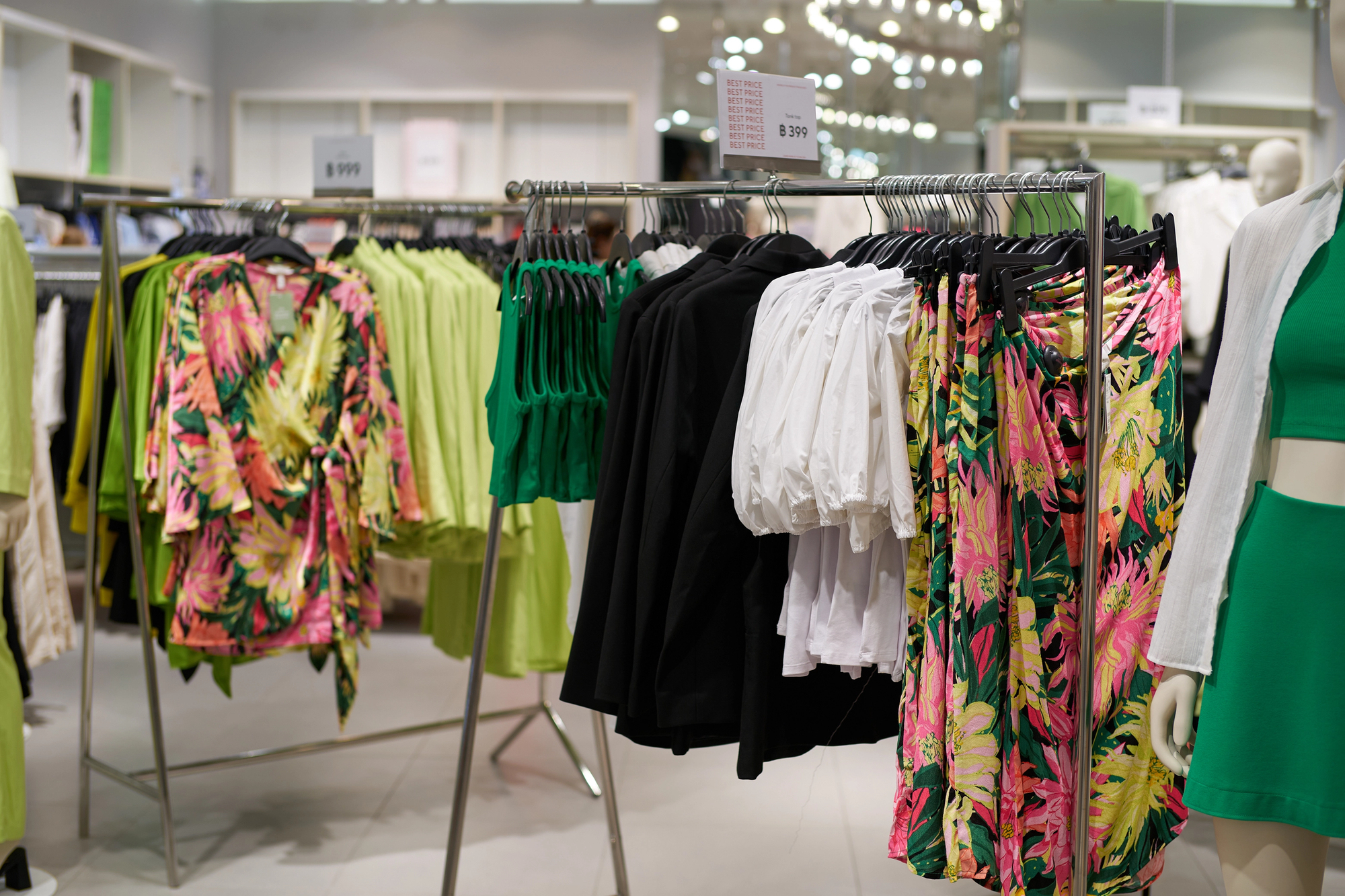 Clothing racks in a store display with green and floral dresses on hangers.