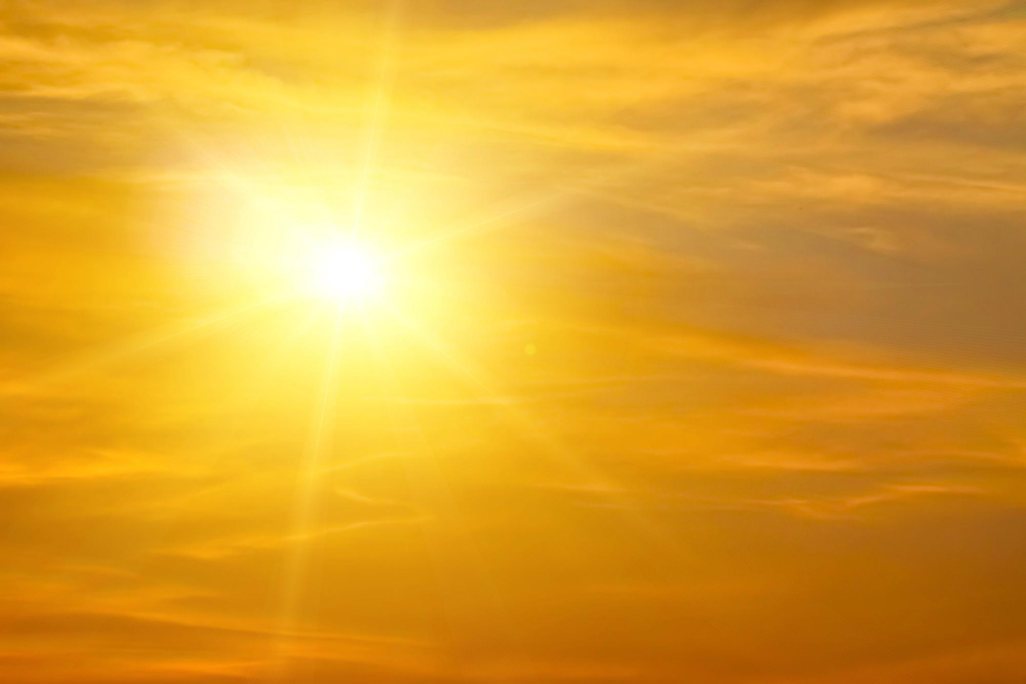 Bright sun in a golden orange sky with wispy clouds spreading warm light.