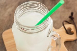 Close-up of a glass milk jar with a bright green straw on a wooden table.