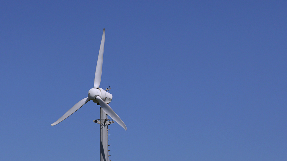 Wind turbine perched on a tall pole against a clear blue sky, illustrating renewable energy.
