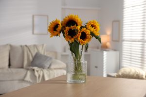 Sunflowers in a textured glass vase on a wooden table in a bright living room.