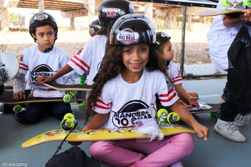 Young brazilian girl sits cross legged outside with skateboard in her lap