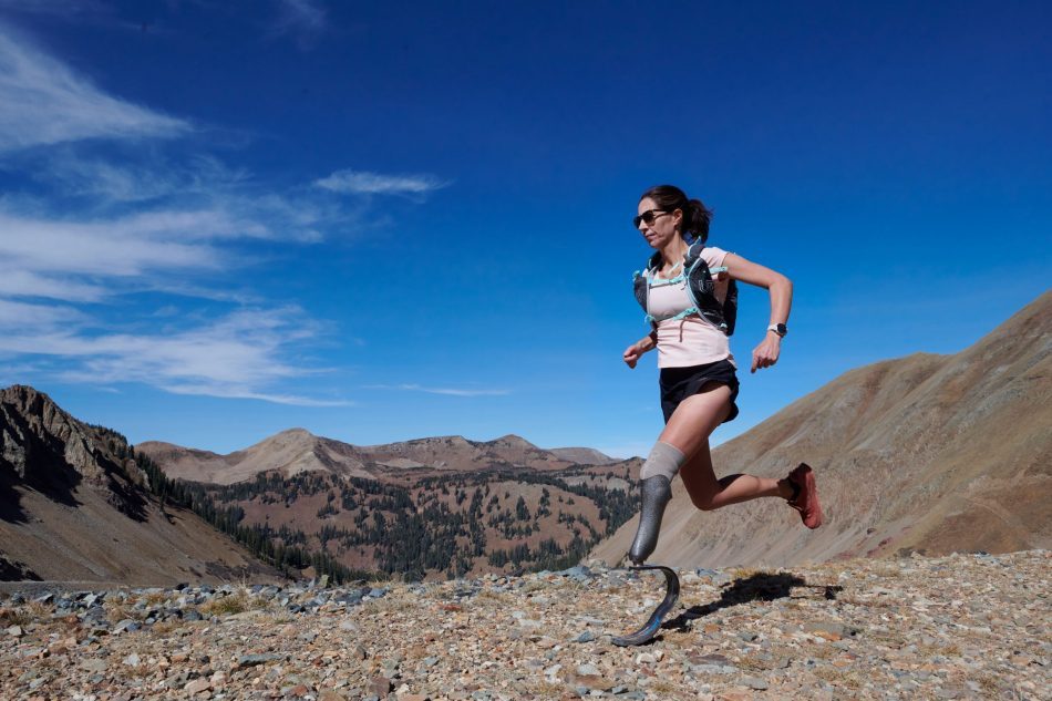Jacky Hunt-Boersma running through a mountain range in front of a blue sky.