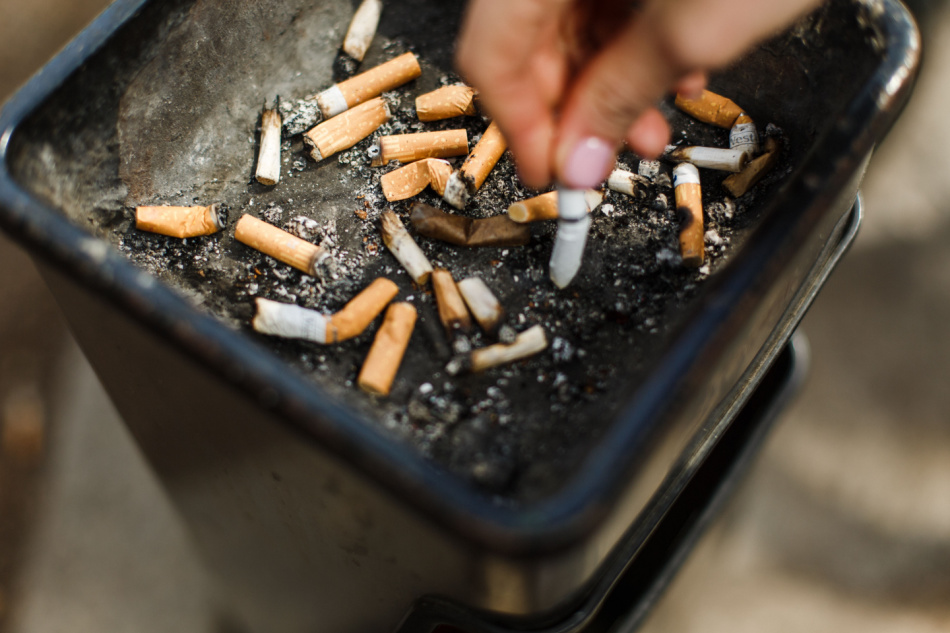 Big ashtray with cigarette butts. A smoker shakes off the ash in an ashtray.