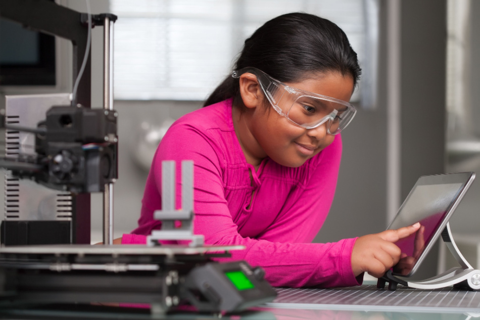 A young girl wearing pink is working on a touchscreen making changes to a 3d printed toy in a summer school tech class.