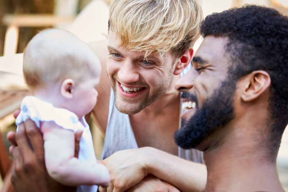 Loving Male Interracial Same Sex Couple Cuddling Baby Daughter At Home In Garden Together