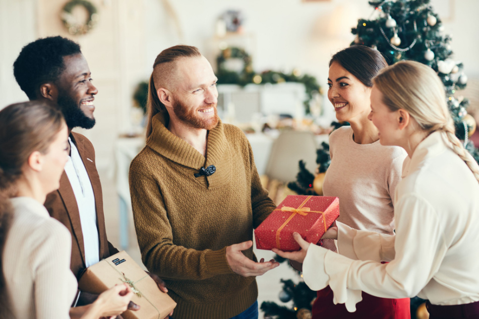Group of elegant diverse young people exchanging gifts and smiling cheerfully during Christmas party