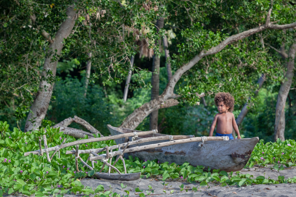 Tanna, Vanuatu - June 2019: Melanesian boy in traditional wooden outrigger boat on the beach green rain forest