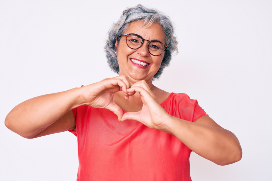 Senior hispanic grey- haired woman wearing casual clothes and glasses smiling in love doing heart symbol shape with hands.