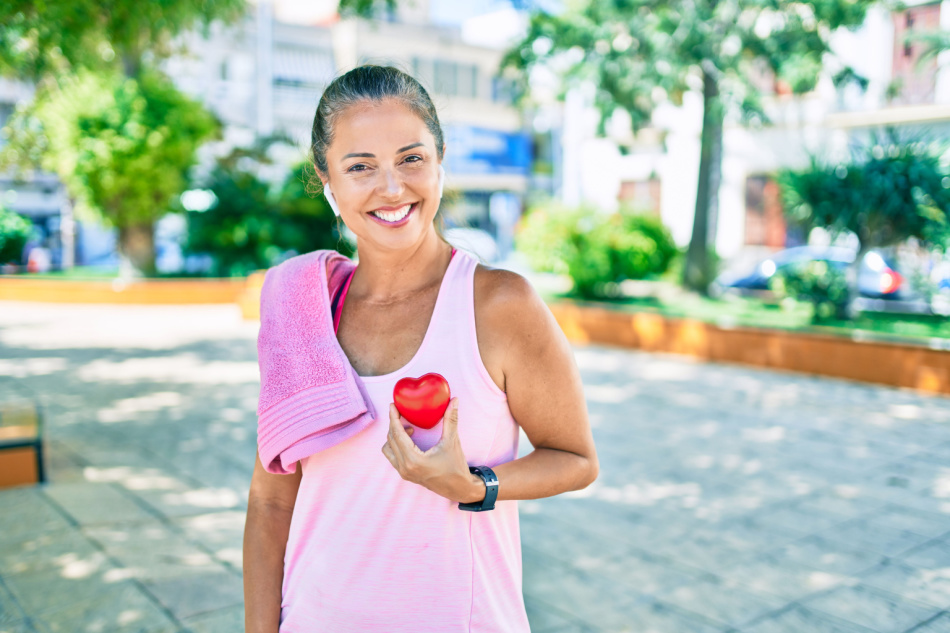 Middle age sportswoman health care holding heart at the park