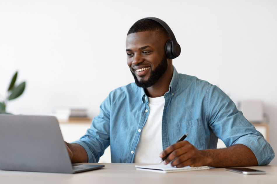 young attractive Black man In Headphones on Laptop video conference Taking Notes