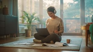 Young Woman Using Laptop at Home, Does Remote Work, Listens Music through Headphones.