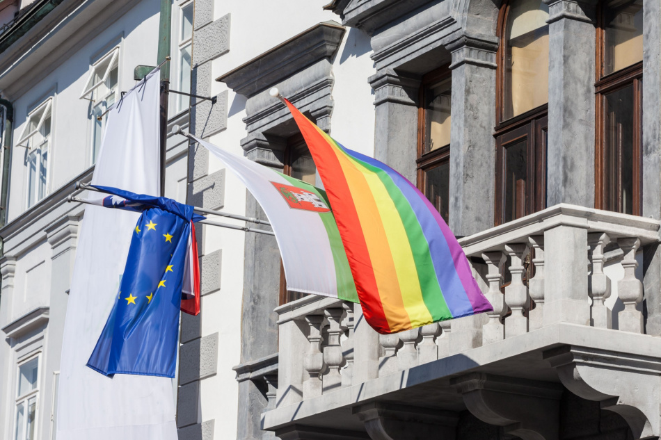 Rainbow lgbtq+ flag next to a flag of the city of Ljubljana, Slovenia with the coat of arms of the city and a European banner.
