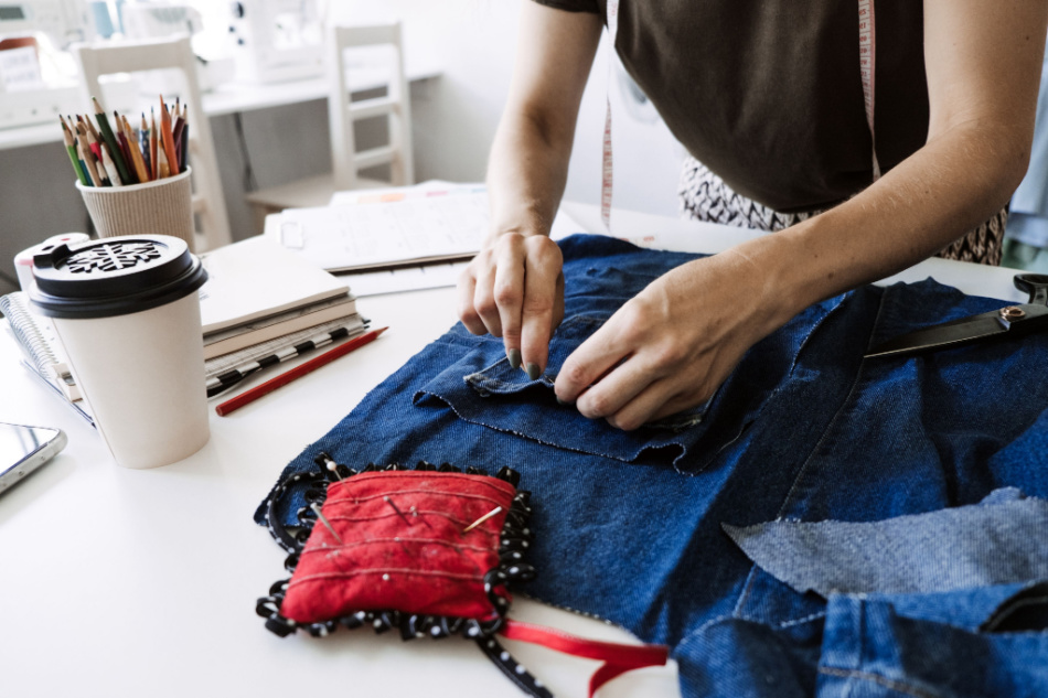 Woman seamstress cut and repairs old blue jeans